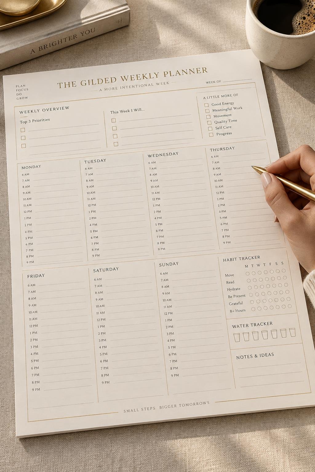 The Gilded Weekly Planner on an ivory linen desk, a woman's hand holding a gold pen, coffee and natural window light — concept mockup